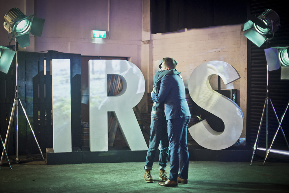 Two people hugging in front of large letters which read "iris" at Iris Prize LGBT+ Film Festival 2017